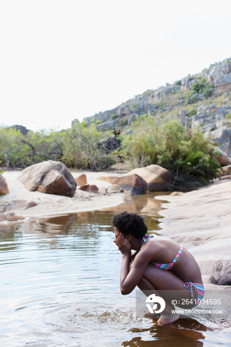 Young woman in bikini splashing water on face at lake