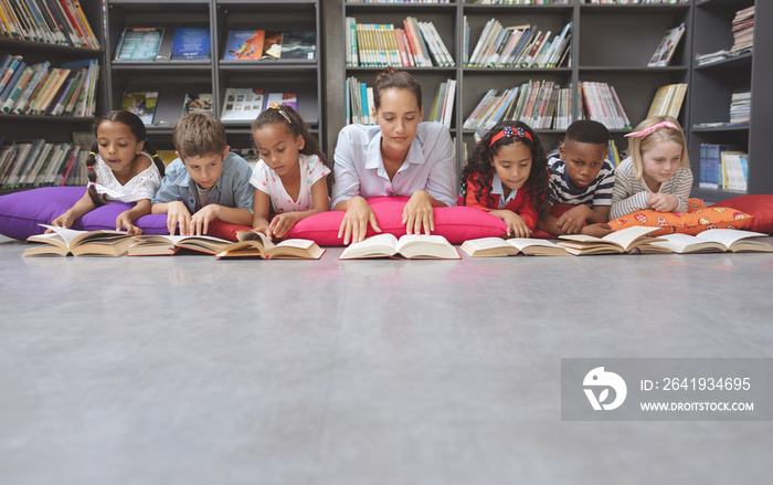 Schoolteacher reading books with his school kids in library