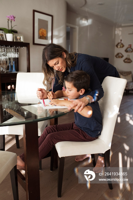 Side view of mother assisting son in writing homework on table at home