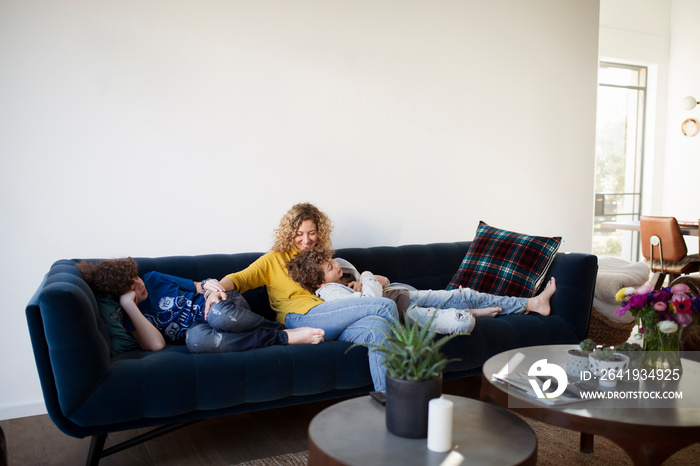 Smiling mother with sons relaxing on sofa against wall at home