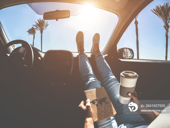 Woman drinking coffee paper cup inside car with feet on dashboard - Girl relaxing in auto trip readi