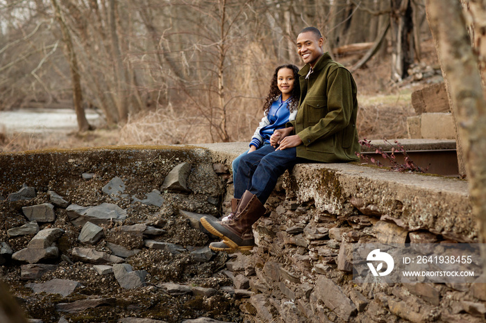 Father and daughter sitting on stone wall