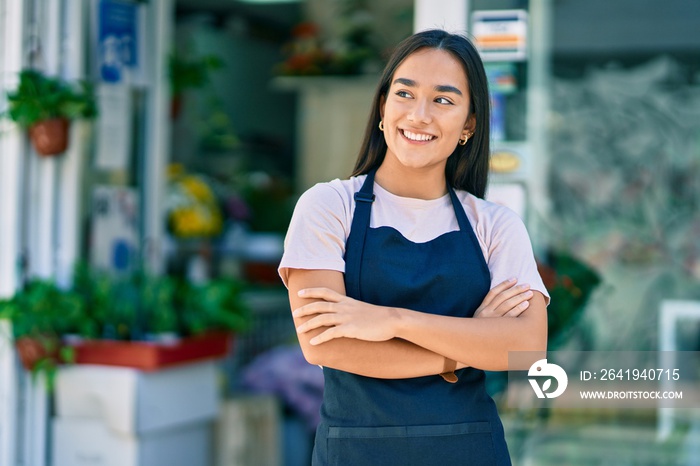 Young latin shopkeeper girl with arms crossed smiling happy standing at the florist