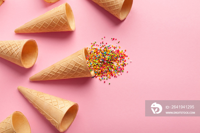 Empty ice-cream waffle cones and colorful sprinkles on pink background,