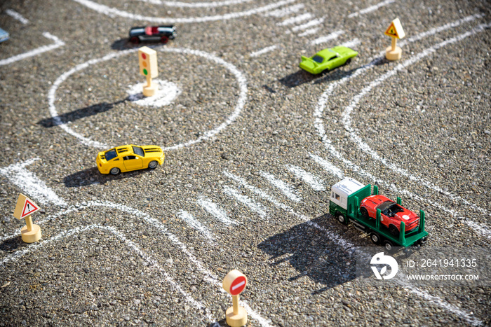 Toy cars red green blue color on the road chalked on black asphalt. Difficult traffic rules concept