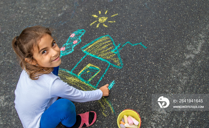 The child draws with chalk on the asphalt. Selective focus.