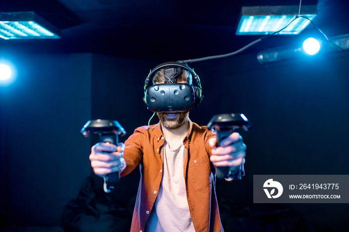 Man playing game using virtual reality headset and gamepads in the dark room of the playing club