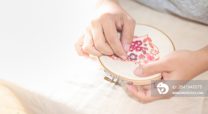 Female hand holding wood embroidery frame and and needle working on flower pattern stitching in a pr