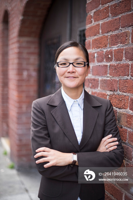 Businesswoman with arms crossed next to brick wall