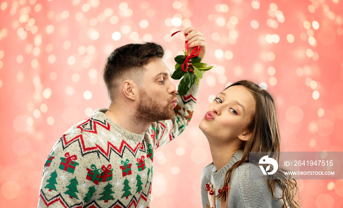 christmas, people and holiday traditions concept - portrait of happy couple in ugly sweaters kissing