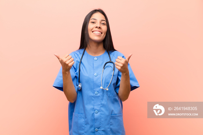 young latin nurse smiling joyfully and looking happy, feeling carefree and positive with both thumbs