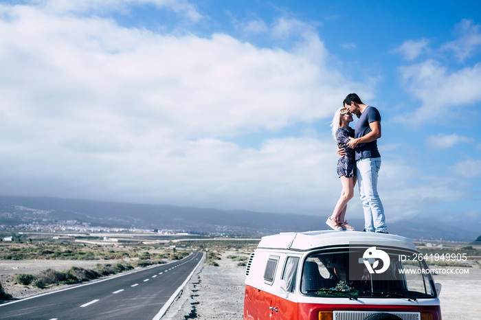 一对热恋中的年轻情侣坐在一辆老式面包车上享受旅行，站在车顶上亲吻拥抱