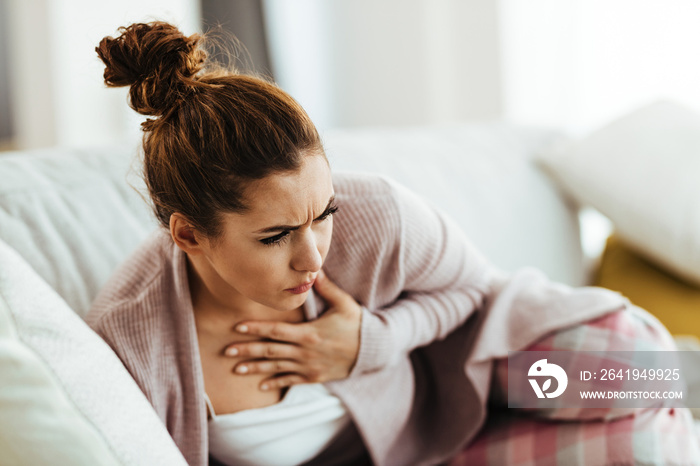 Young woman feeling chest pain while lying down on sofa at home.