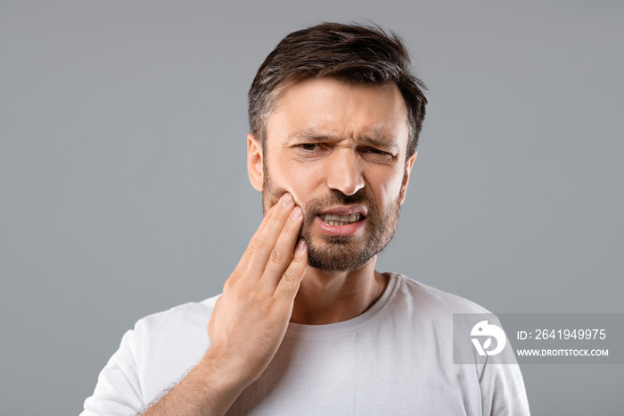 Man suffering from strong tooth pain, grey background