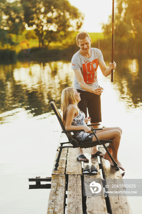 Young happy couple is fishing on the pier at the lake at sunset