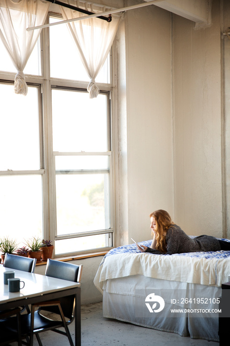 Woman using tablet computer while lying on bed at home