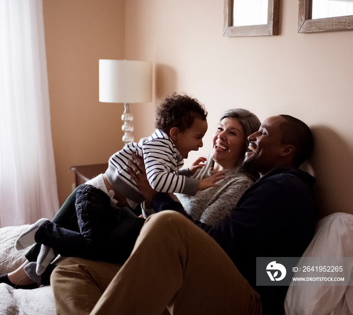 Happy parents playing with cute son while relaxing on bed at home