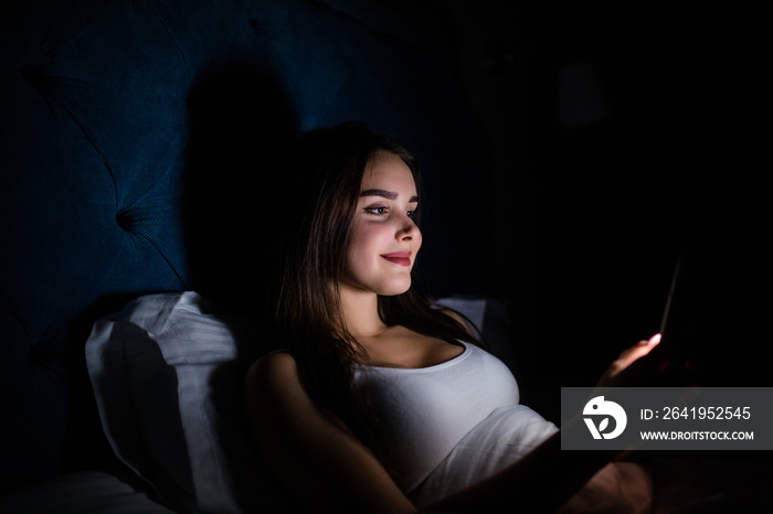 Young woman on bed late at night texting using mobile phone sleepy and tired in internet communicati