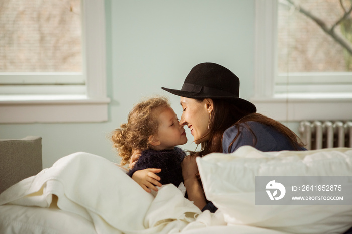 Side view of smiling mother and daughter looking at each other while relaxing on bed