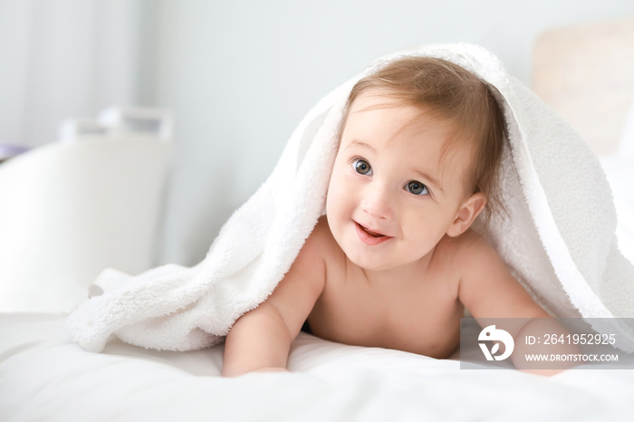 Portrait of adorable baby boy under towel on bed