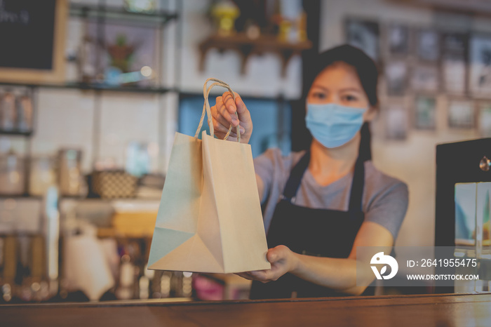 Waitress with medical mask giving eco paper bag with take away food in cafe.