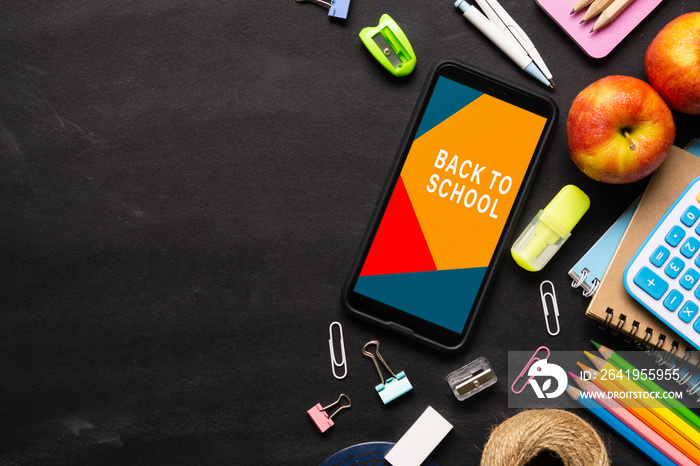 Mock up mobile phone for back to school background concept. School items on black chalkboard backgro