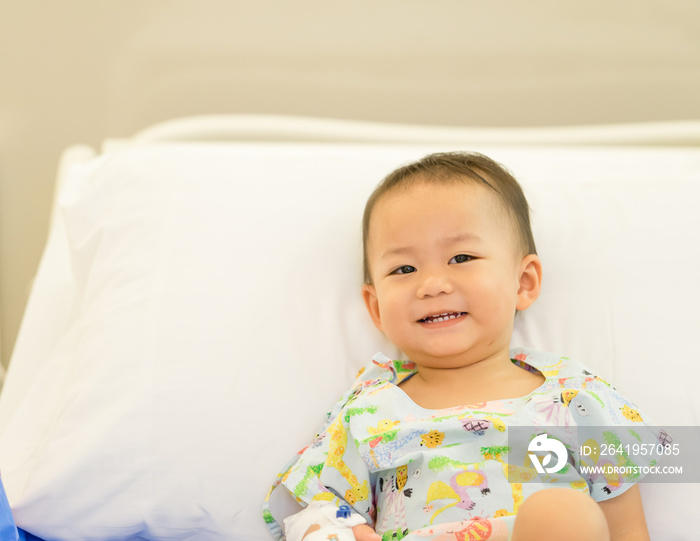 Sick child baby boy lying in bed with a fever and smile in the bed at hospital.