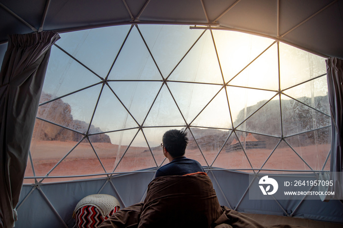 Tourist man staying in blanket in dome tent looking outside at Wadi Rum desert, famous natural attra