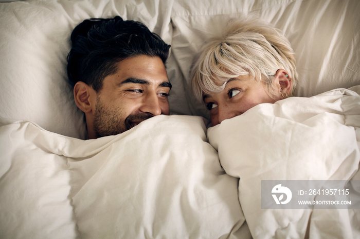 Young couple lying in bed under blanket