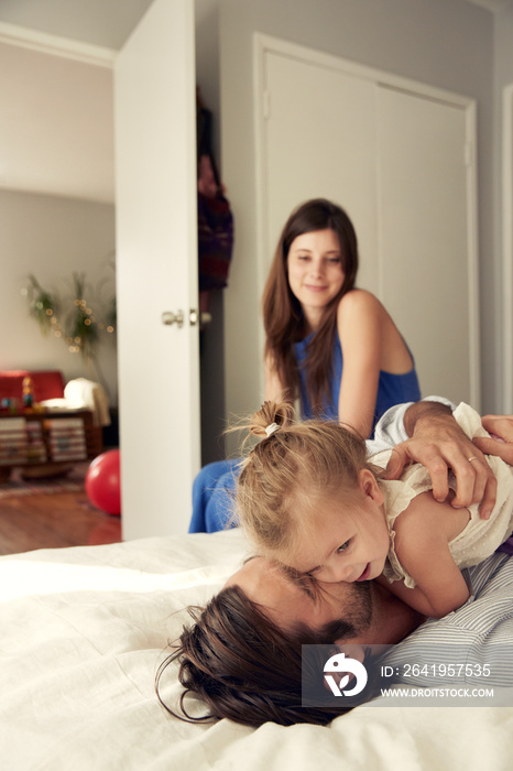 Father playing with daughter on bed with mother sitting on background