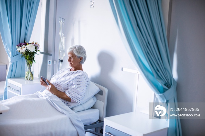 Female senior patient using mobile phone on bed