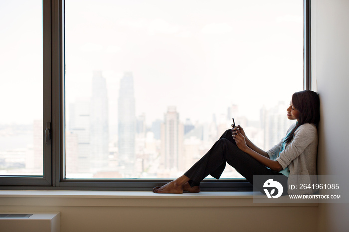 Woman sitting on windowsill using smartphone