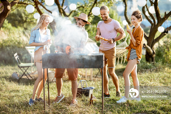 Group of a young friends having barbecue, cooking food in the beautiful garden during a festive lunc