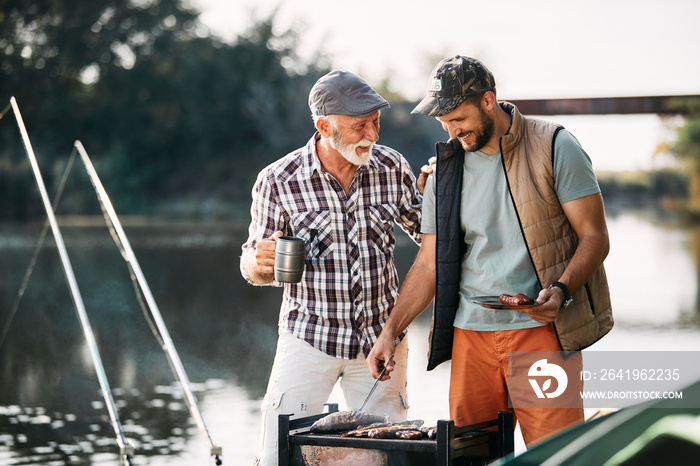 一个快乐的成熟男人在大自然中露营时，与正在烧烤烤鱼的儿子交谈。
