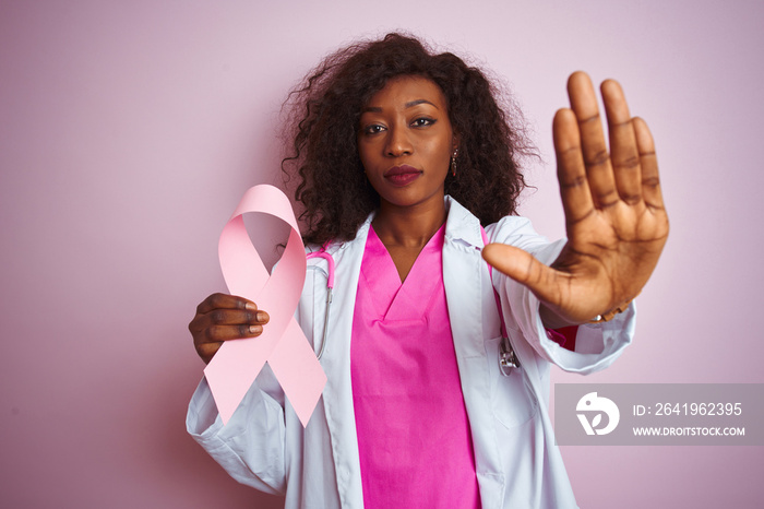 Young african american doctor woman holding cancer ribbon over isolated pink background with open ha