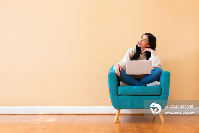 Young woman with a laptop computer in a thoughtful pose sitting in a chair