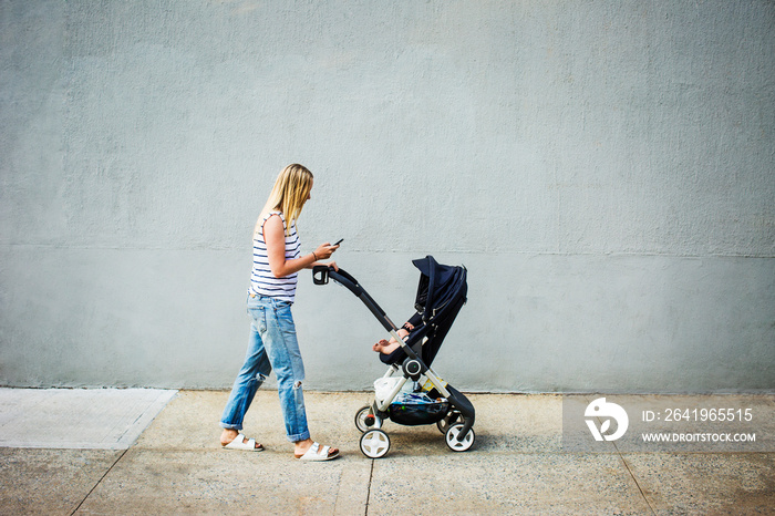 Mother with baby girl (6-11 months) in stroller walking on sidewalk