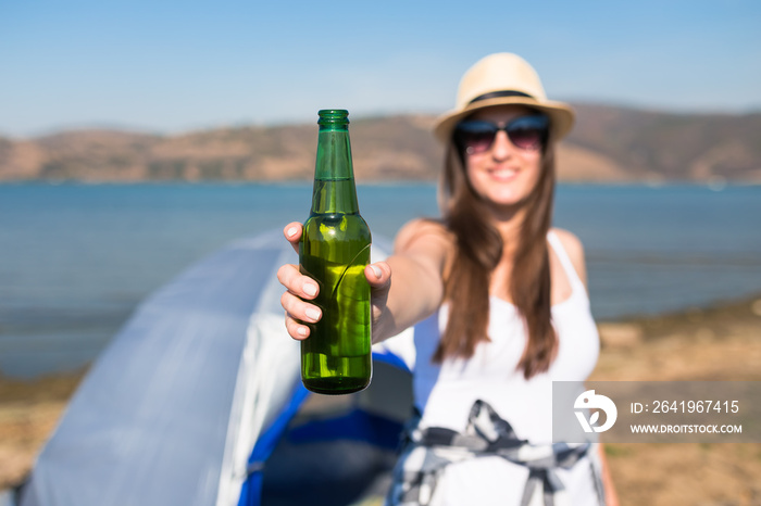 Close up of modern woman holding beer bottle next to tent outdoors. Camping and freedom concept.