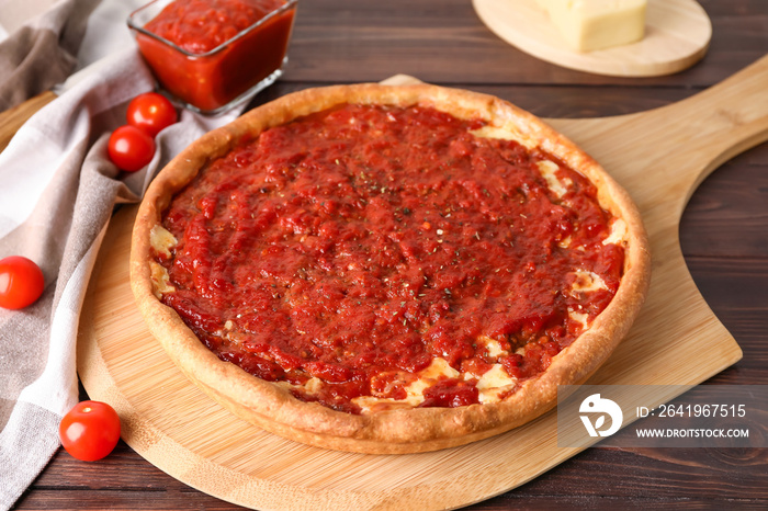 Board with tasty Chicago-style pizza, sauce and tomatoes on wooden background