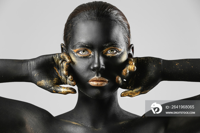 Beautiful woman with black and golden paint on her body against light background