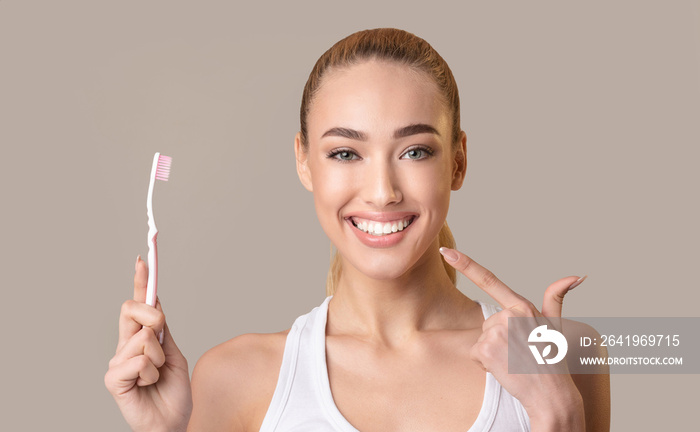 Girl Pointing Finger At Smile Holding Toothbrush Over Beige Background