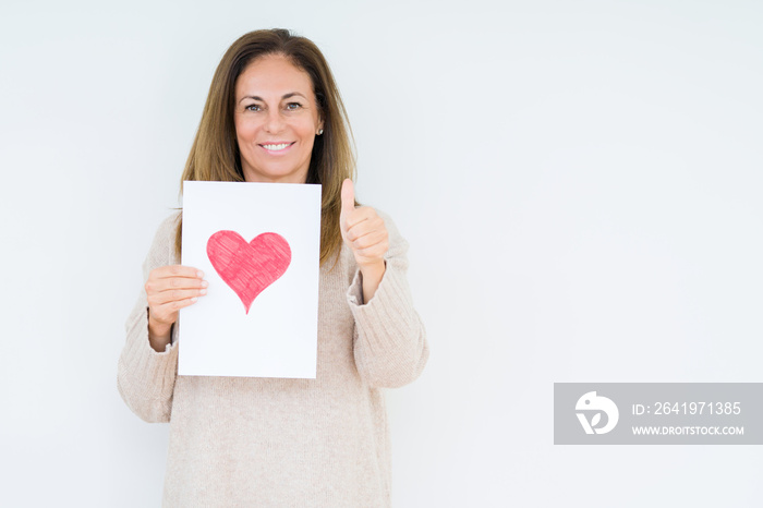 Middle age woman holding card gift with red heart over isolated background happy with big smile doin