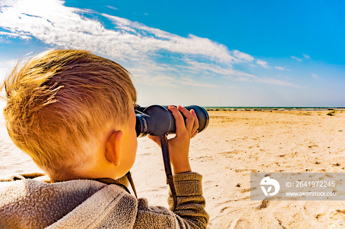 A boy with binoculars looks into the sea, the concept of the future search for his place in life.