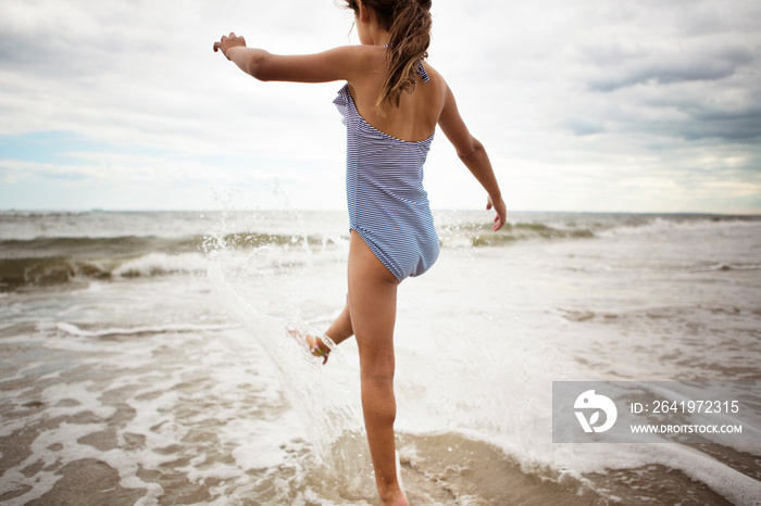 Little girl (6-7) playing with waves on beach rear view