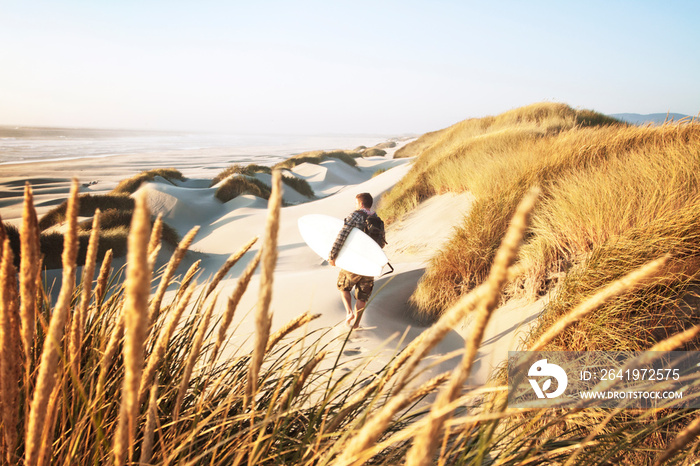 Man walking through sand dunes with surfboard