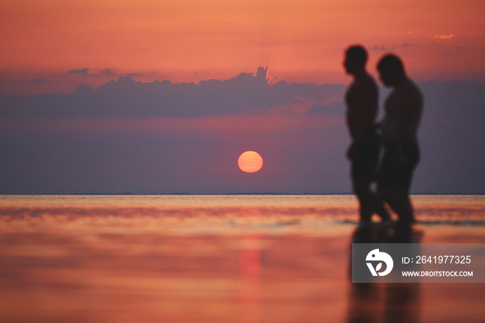 silhouettes of two men against the sea and sunset. happy man enjoying summer vacation