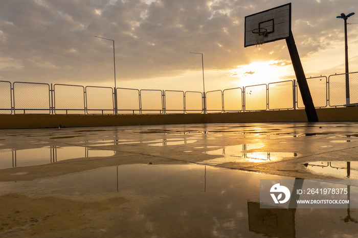 雨后空旷潮湿的篮球场，背景中有水坑反射阳光。