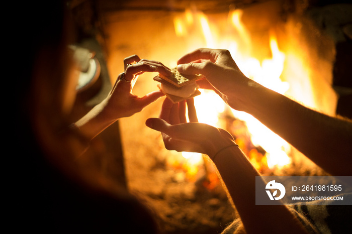 Cropped image of couple holding smores while sitting near to campfire at night