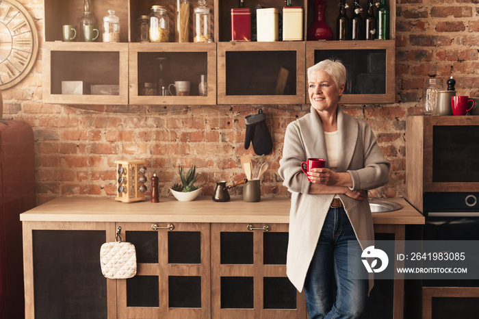 Dreamy senior woman enjoying coffee at kitchen