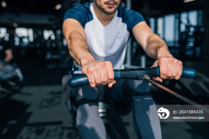 Cropped image of a muscular man using rowing machine in the gym.